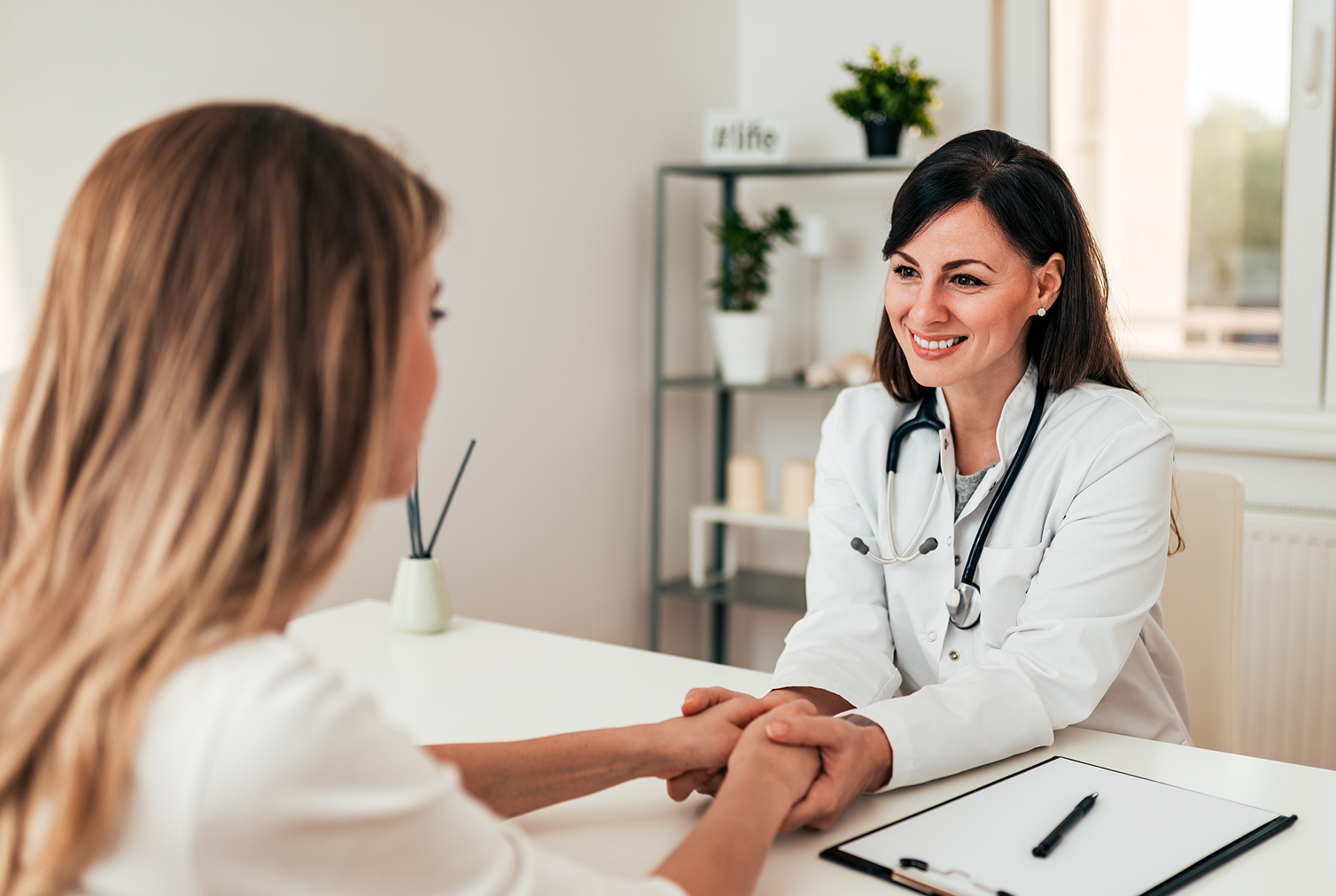 Female doctor holding patient's hands and smiling warmly during a consultation